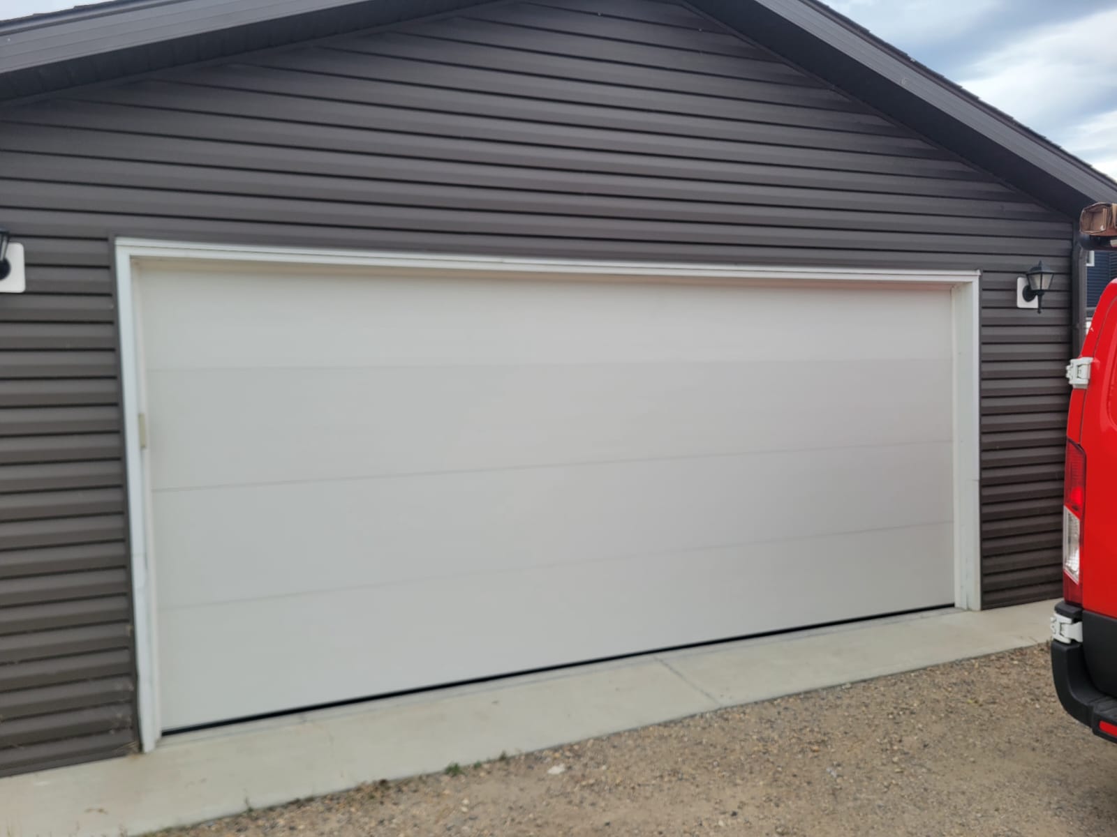 Repaired white sectional garage door on a garage with dark grey siding